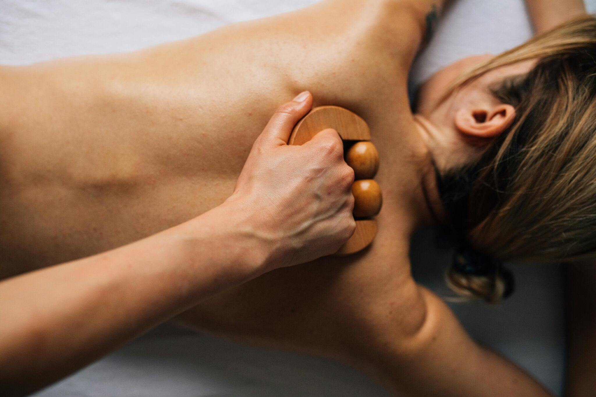 Woman receiving a relaxing back massage with a wooden tool in an indoor, serene setting.
